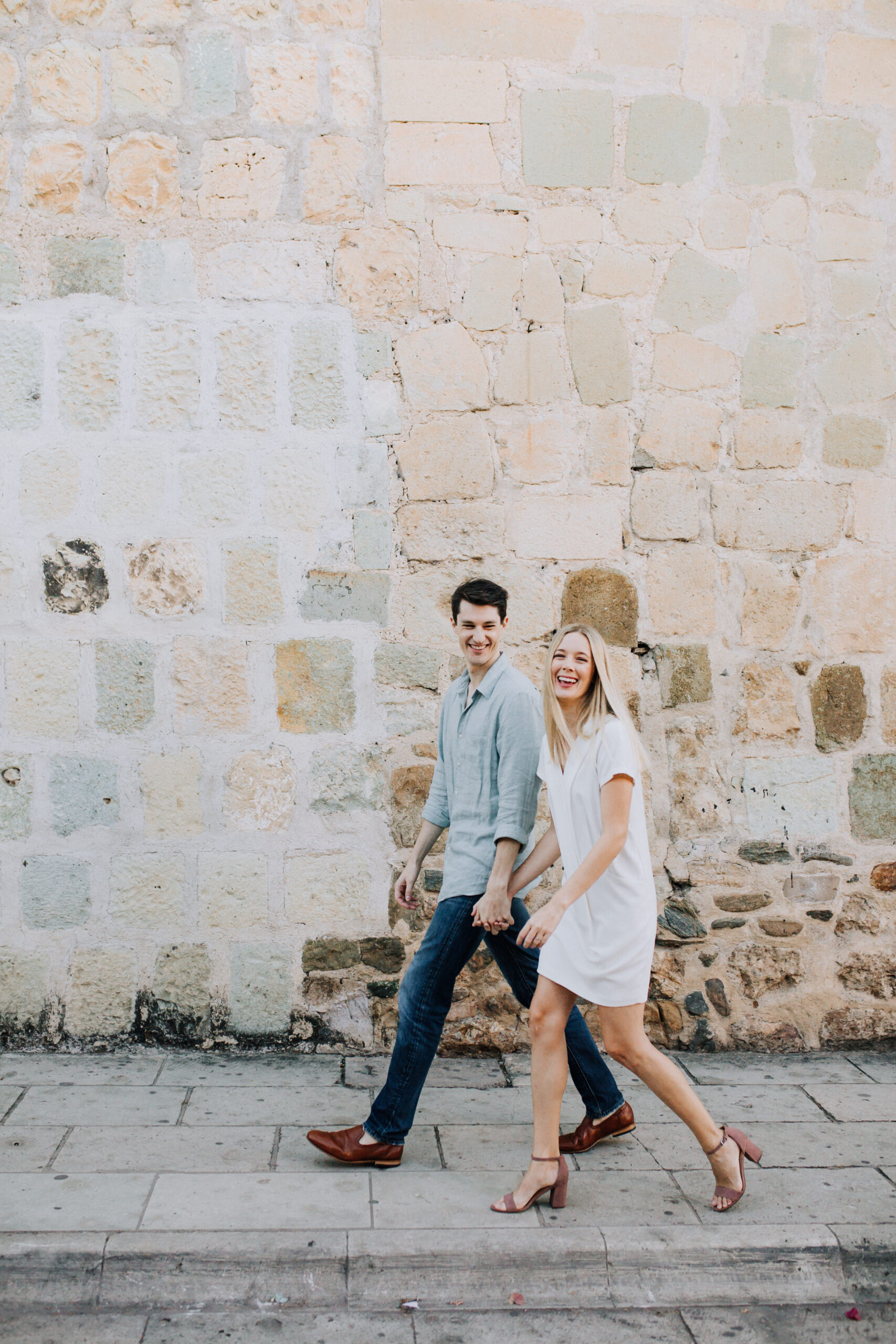 stunning couple walk and take candid engagement photos with a colorful rock wall in the background