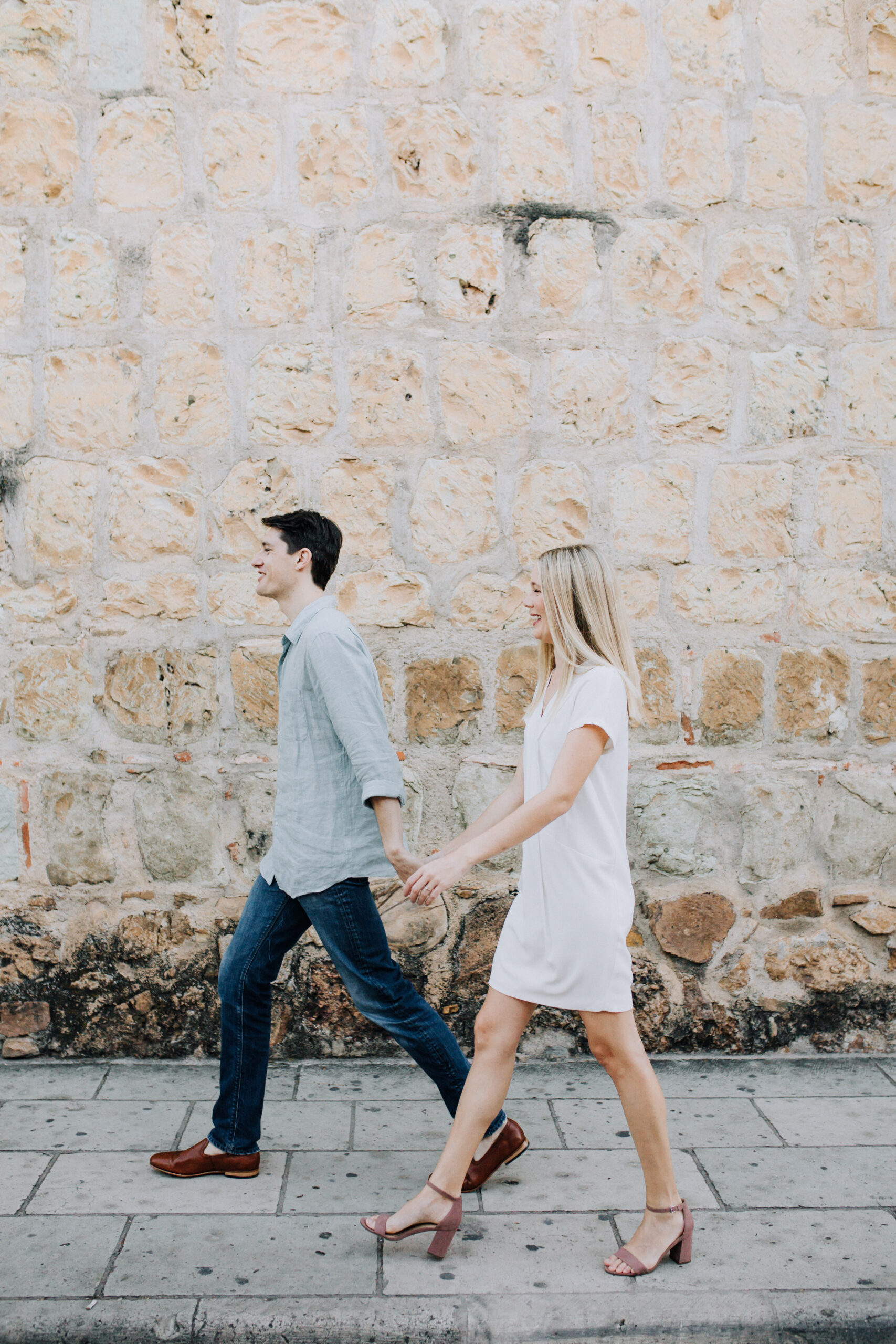 stunning couple walk and take candid engagement photos with a colorful rock wall in the background