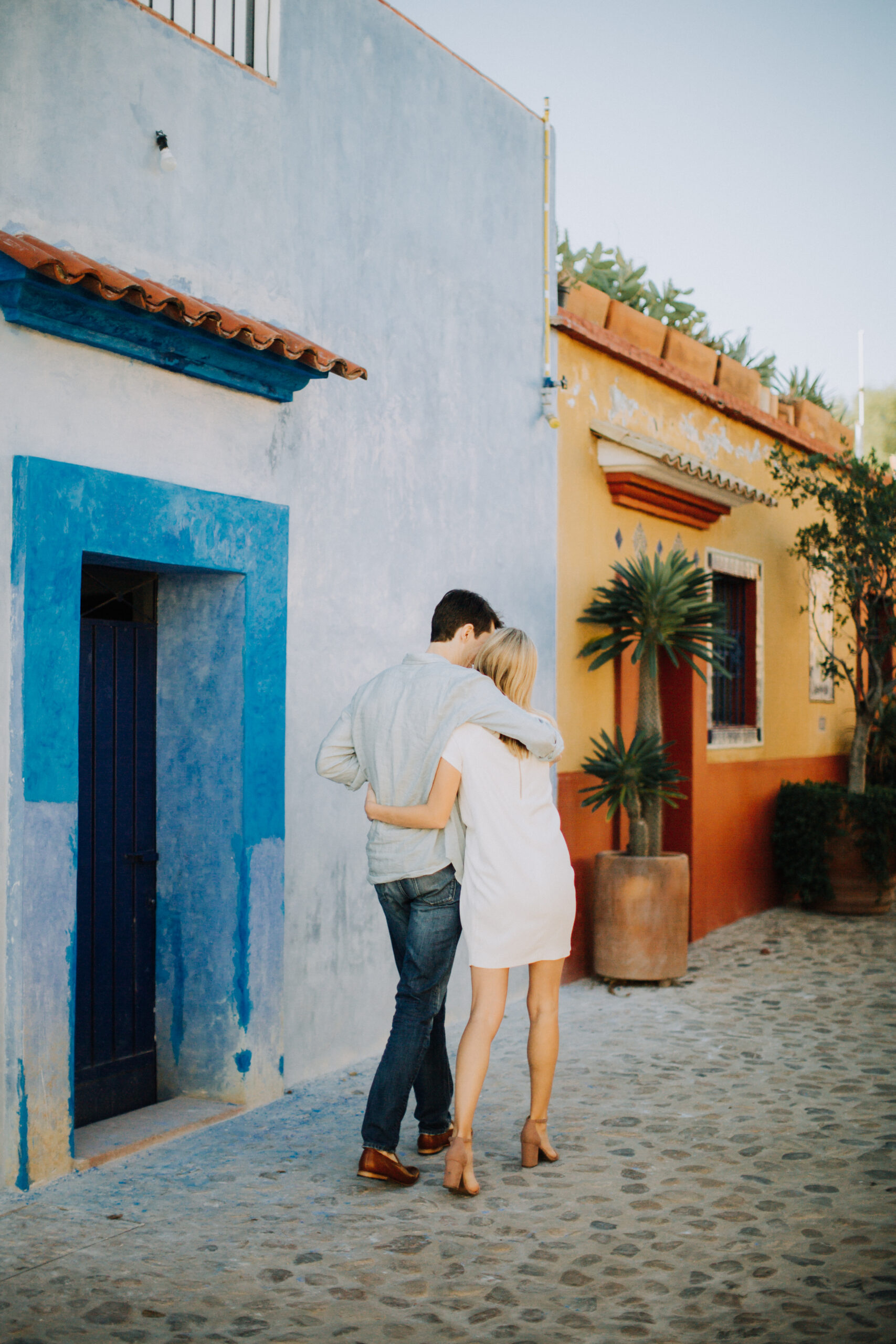 beautiful couple walks with the blue and orange buildings of Oaxaca as a backdrop