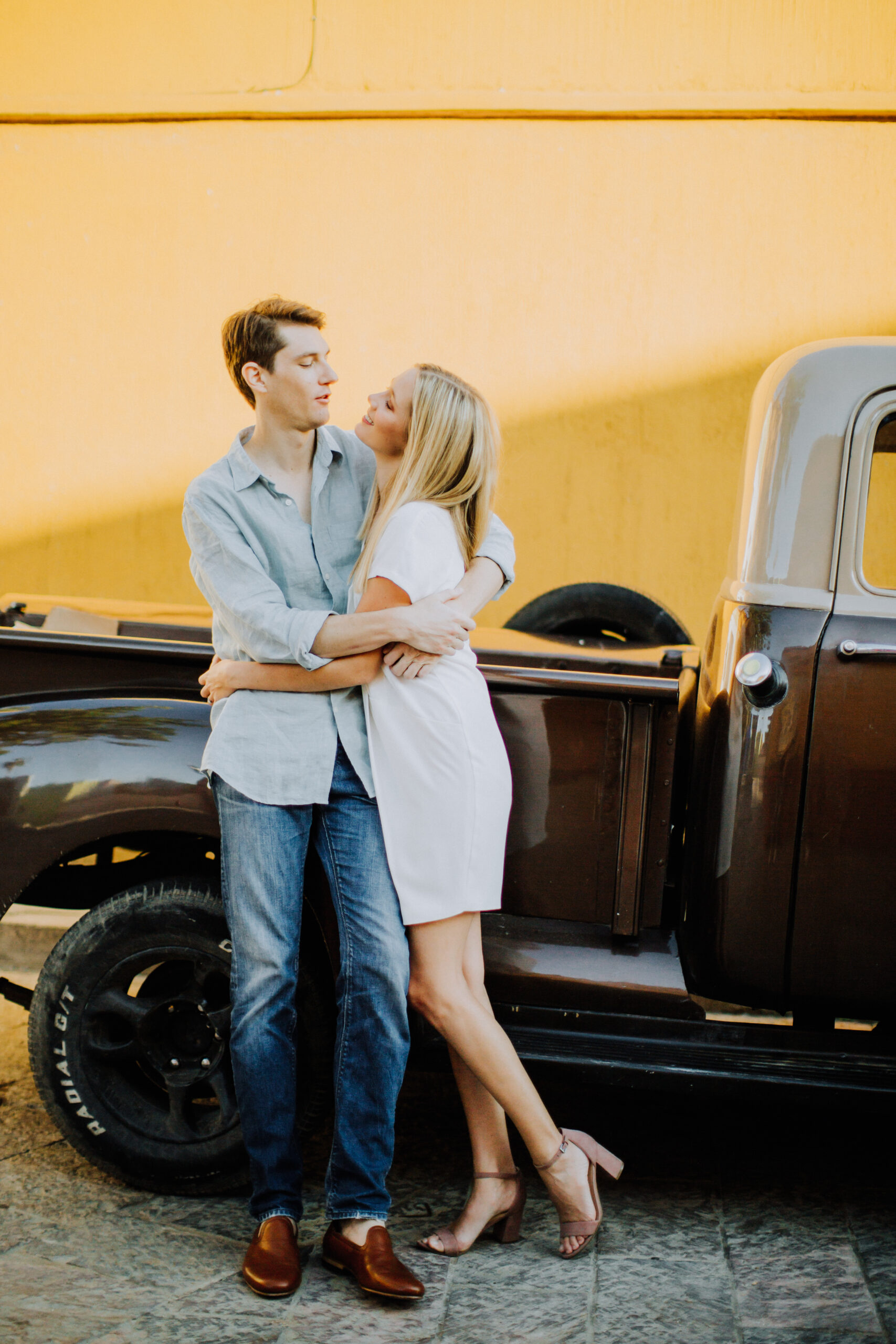 dreamy couple poses with a classic truck against a bright yellow background