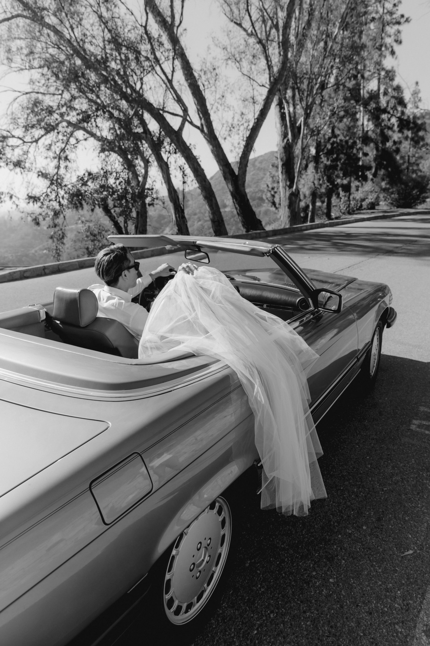 bride and groom pose together in a convertible overlooking the LA mountains
