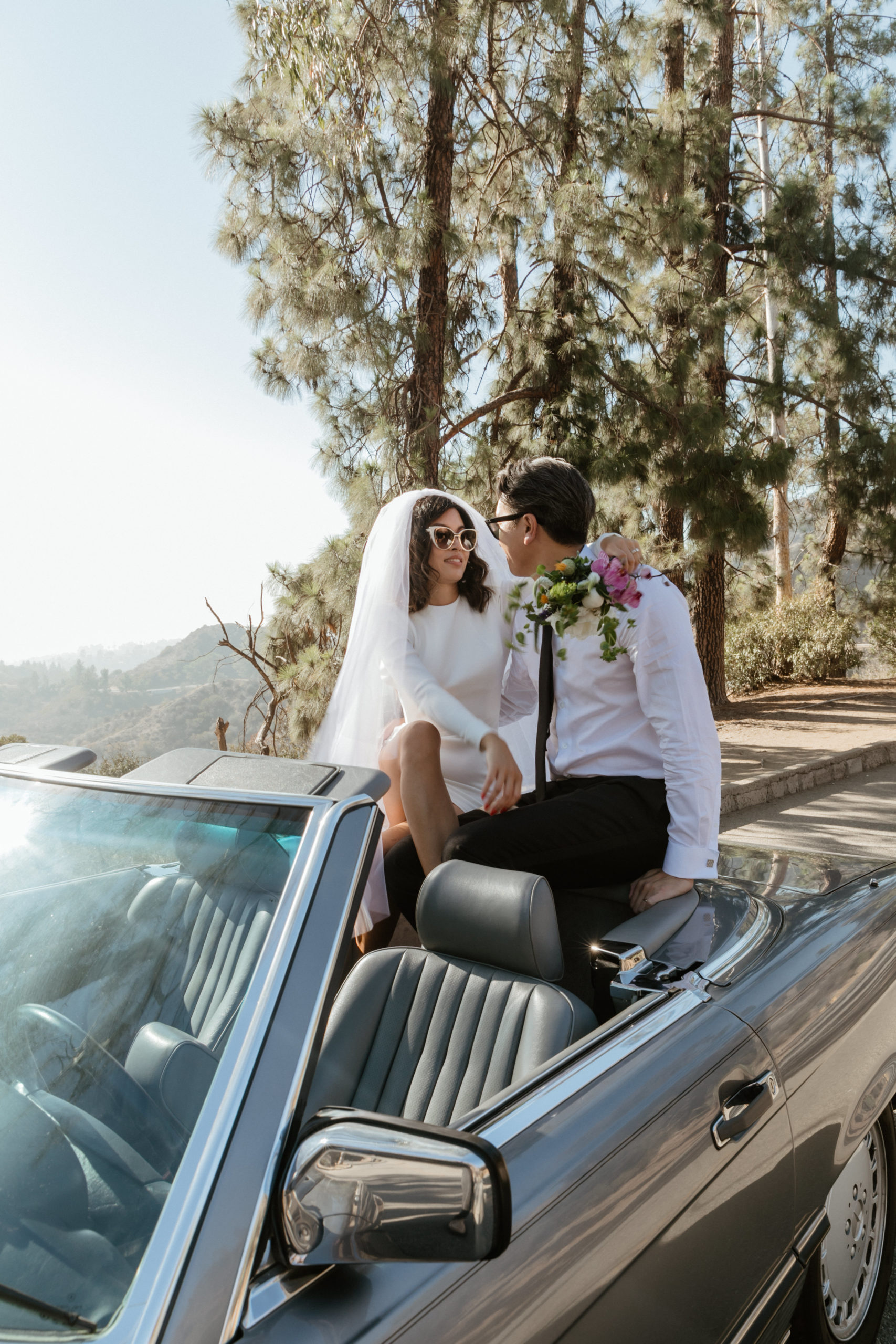 bride and groom pose together in a convertible overlooking the LA mountains