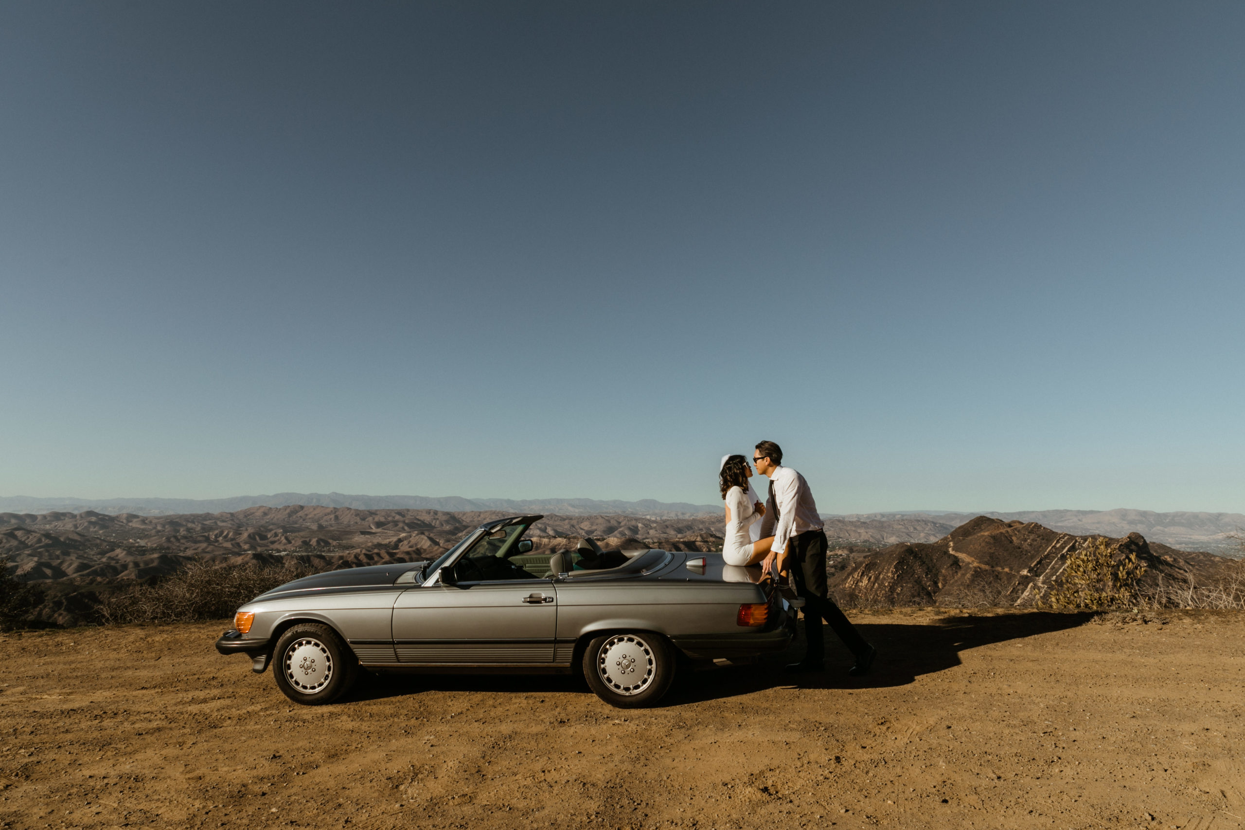 beautiful bride and groom pose beside a convertible together overlooking the LA mountains 
