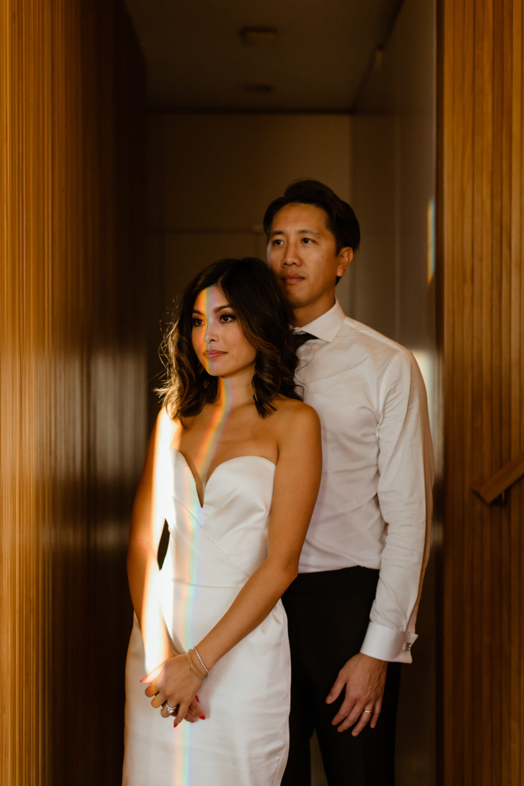 bride and groom pose in their house as the sun gleams through