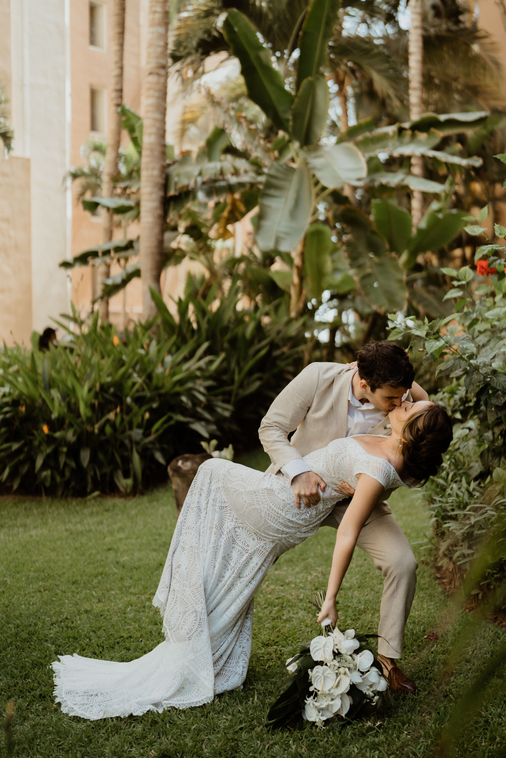 groom dip kissing bride in tropical greenery.