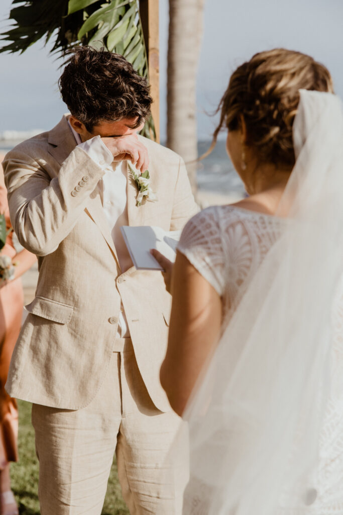 groom crying in tan suit with bride at beach wedding.