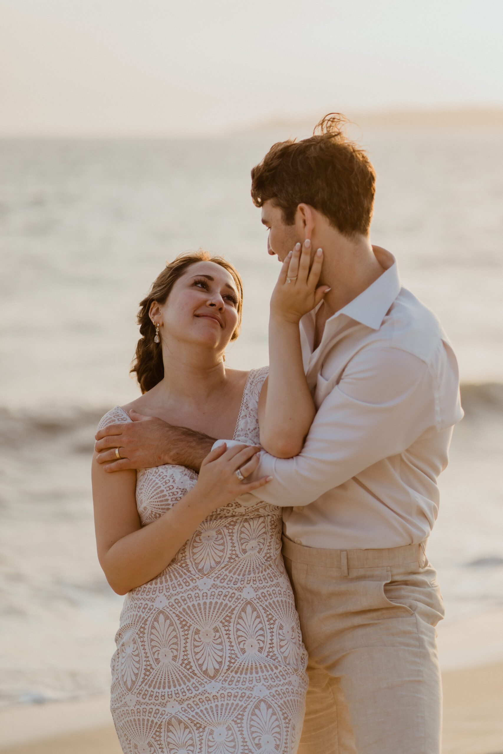 bride holding grooms face on the beach.