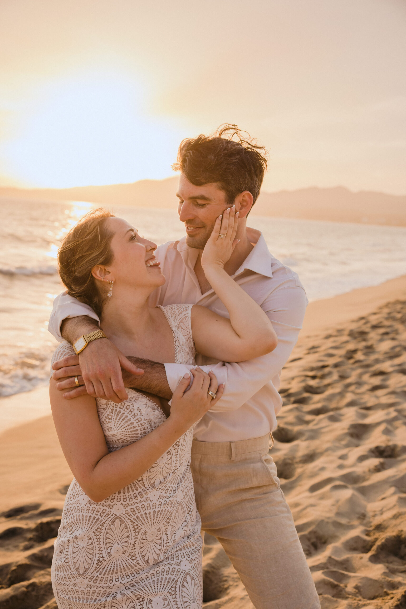 bride and groom hugging each other on beach at sunset.