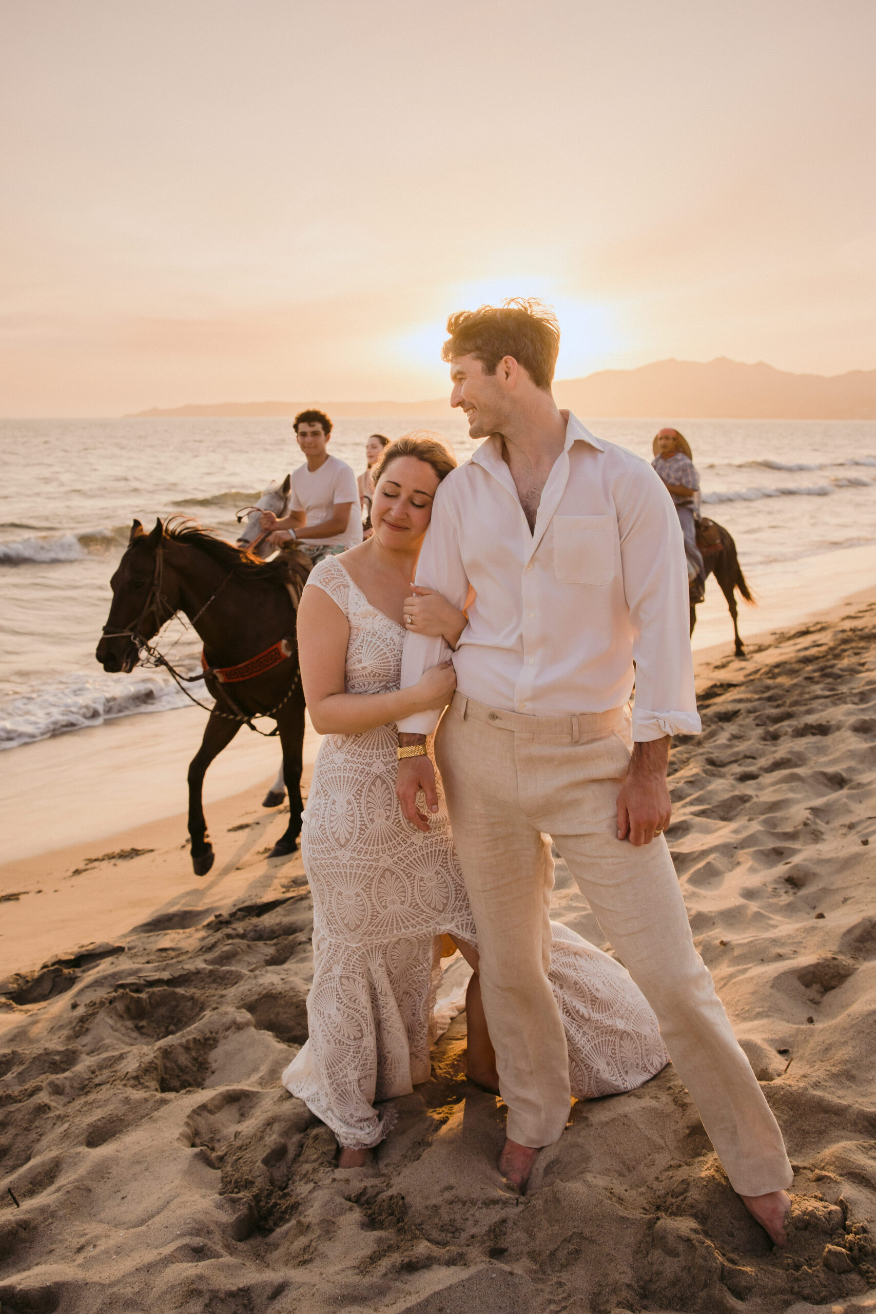bride and groom holding each other on beach with horses.