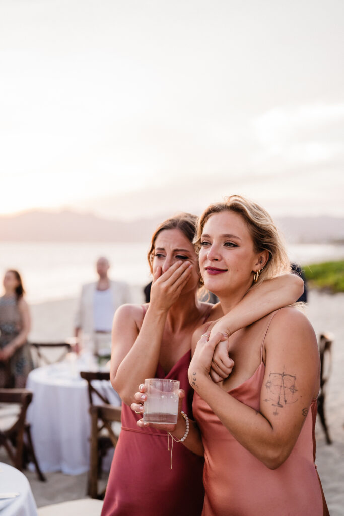 friend wrapping arm around each other on beach at puerto vallarta wedding.