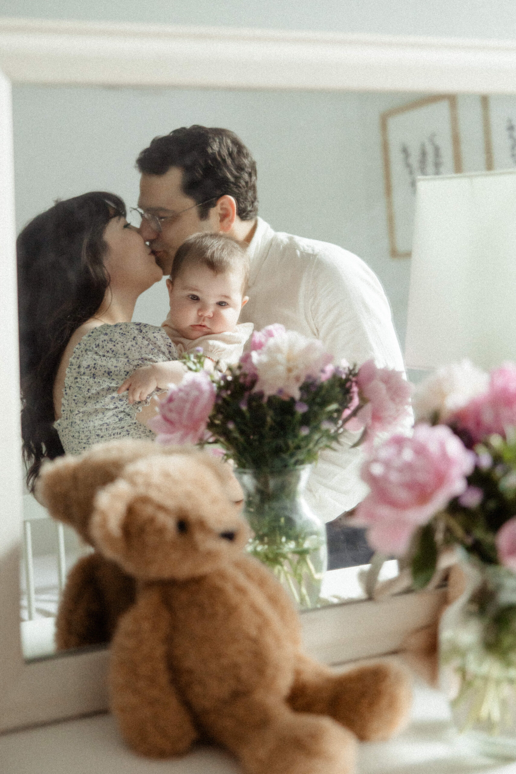 infant girl poses with her mom and dad with a beautiful bouquet of pink flowers