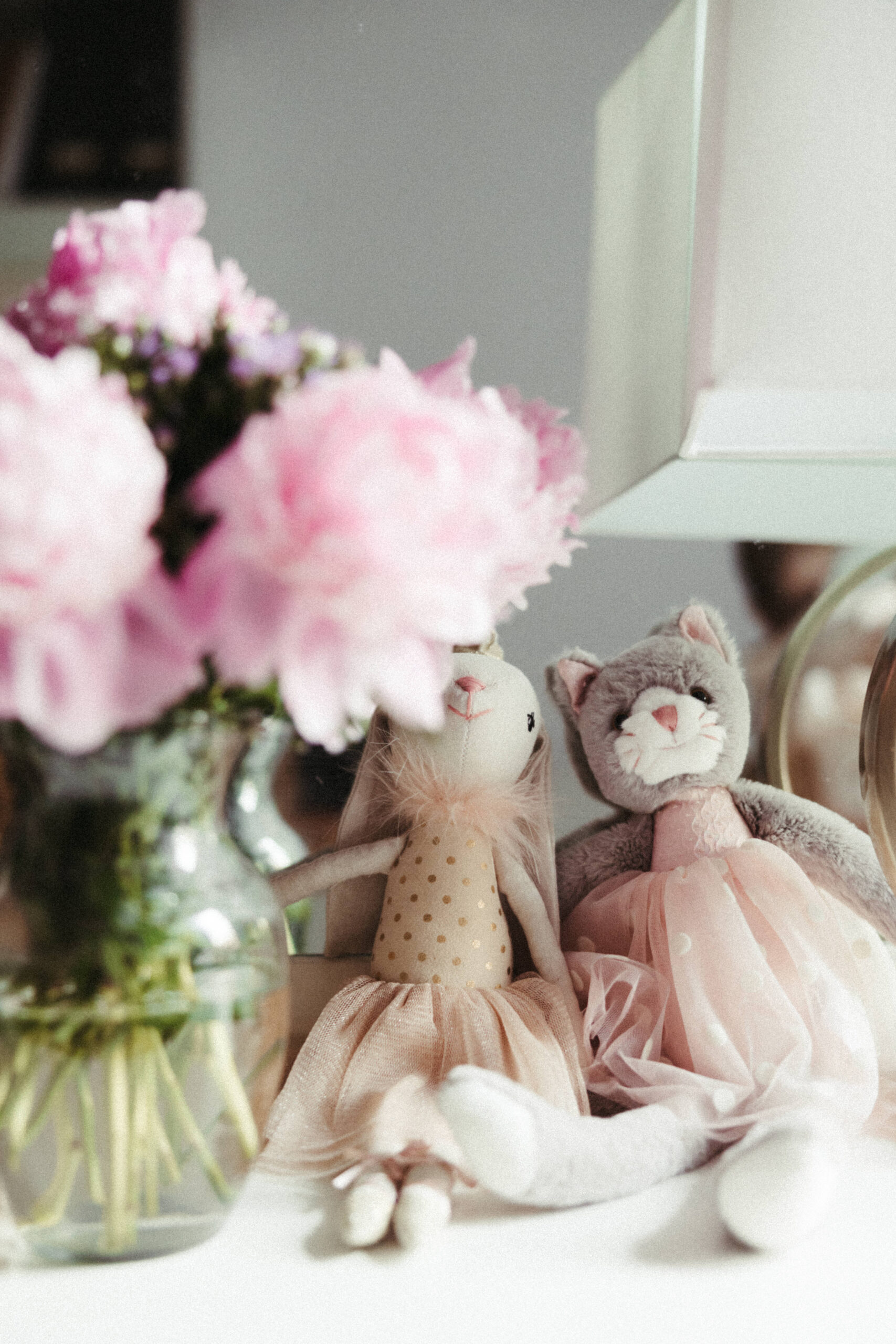 Pink flowers sit with a baby girls teddy bear and rabbit on her nightstand during a candid in home family photo shoot