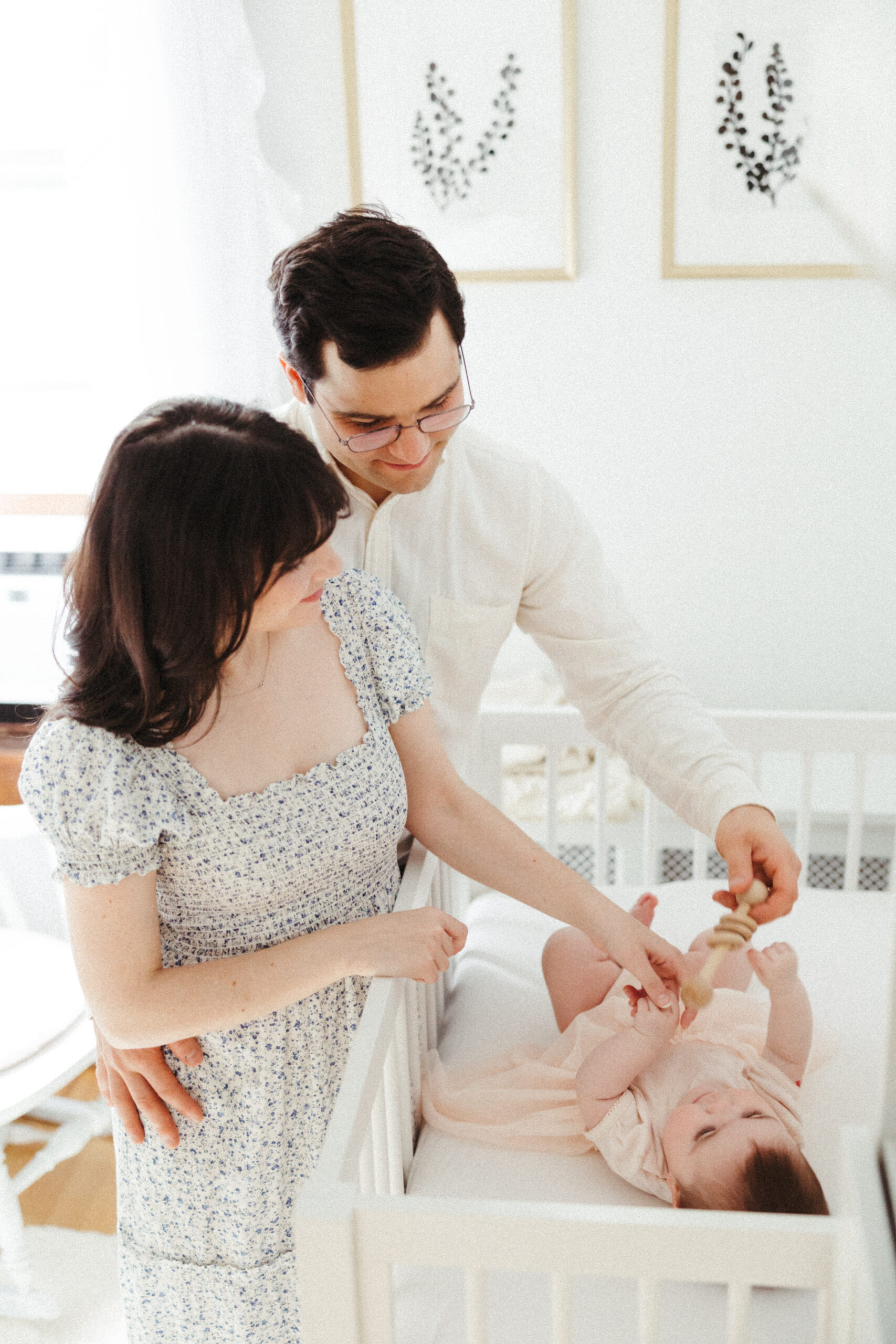 Beautiful infant with mom and dad in their white modern baby room during their in home family photo shoot
