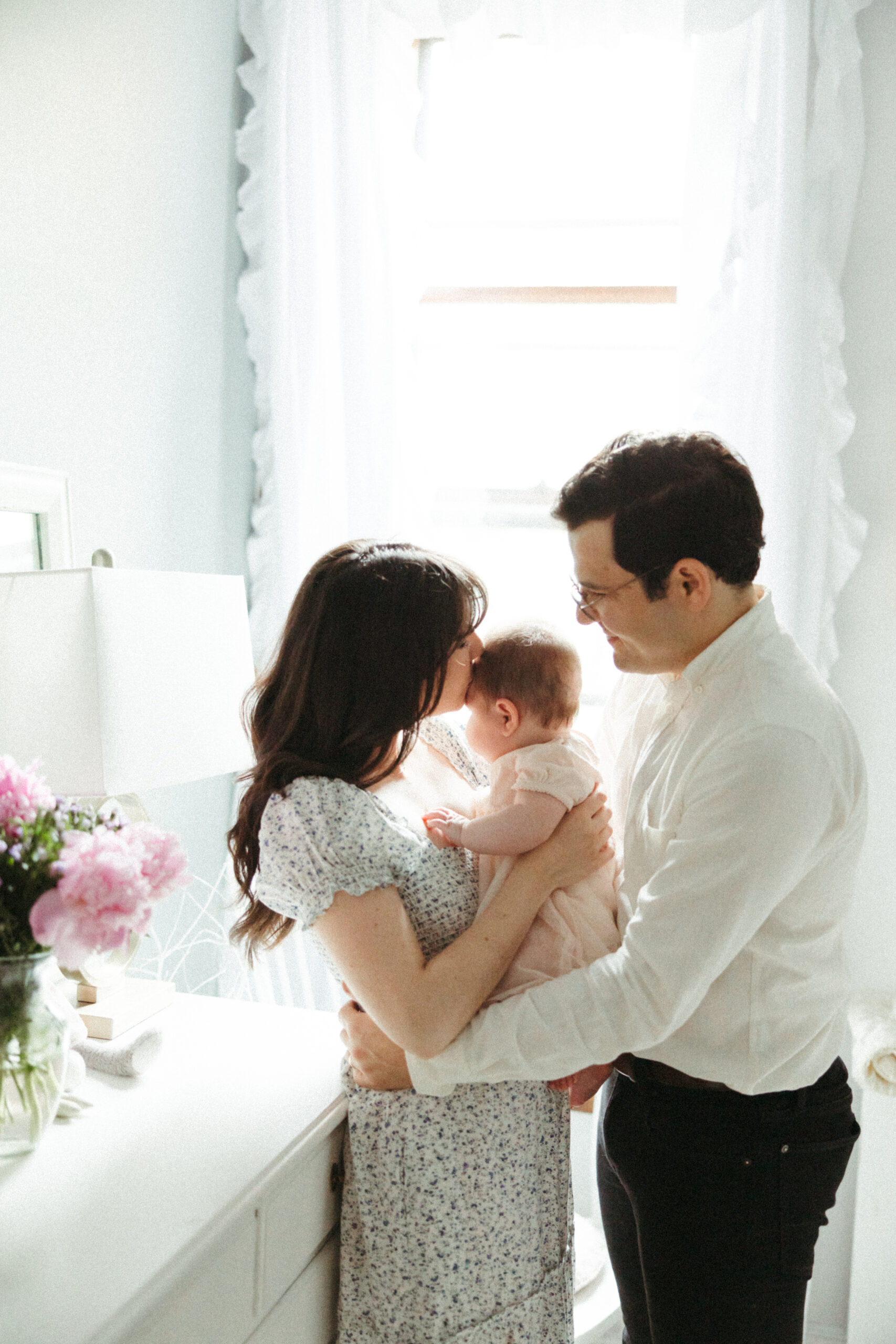 Beautiful infant with mom and dad in their white modern baby room.
