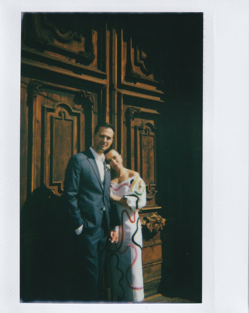 film photo of bride and groom standing in front of brown historic door in Mexico. 
