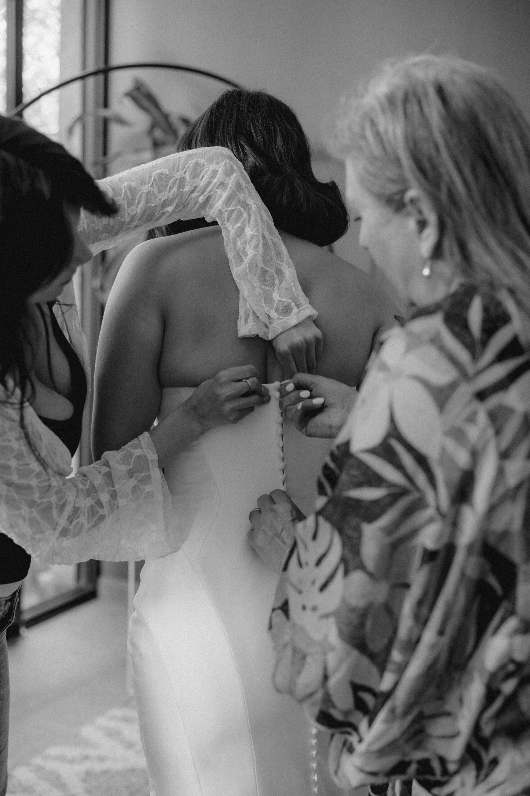 Brides mom and friends help her finish zipping her wedding dress as she preps for her Sobremesa Mexico wedding day