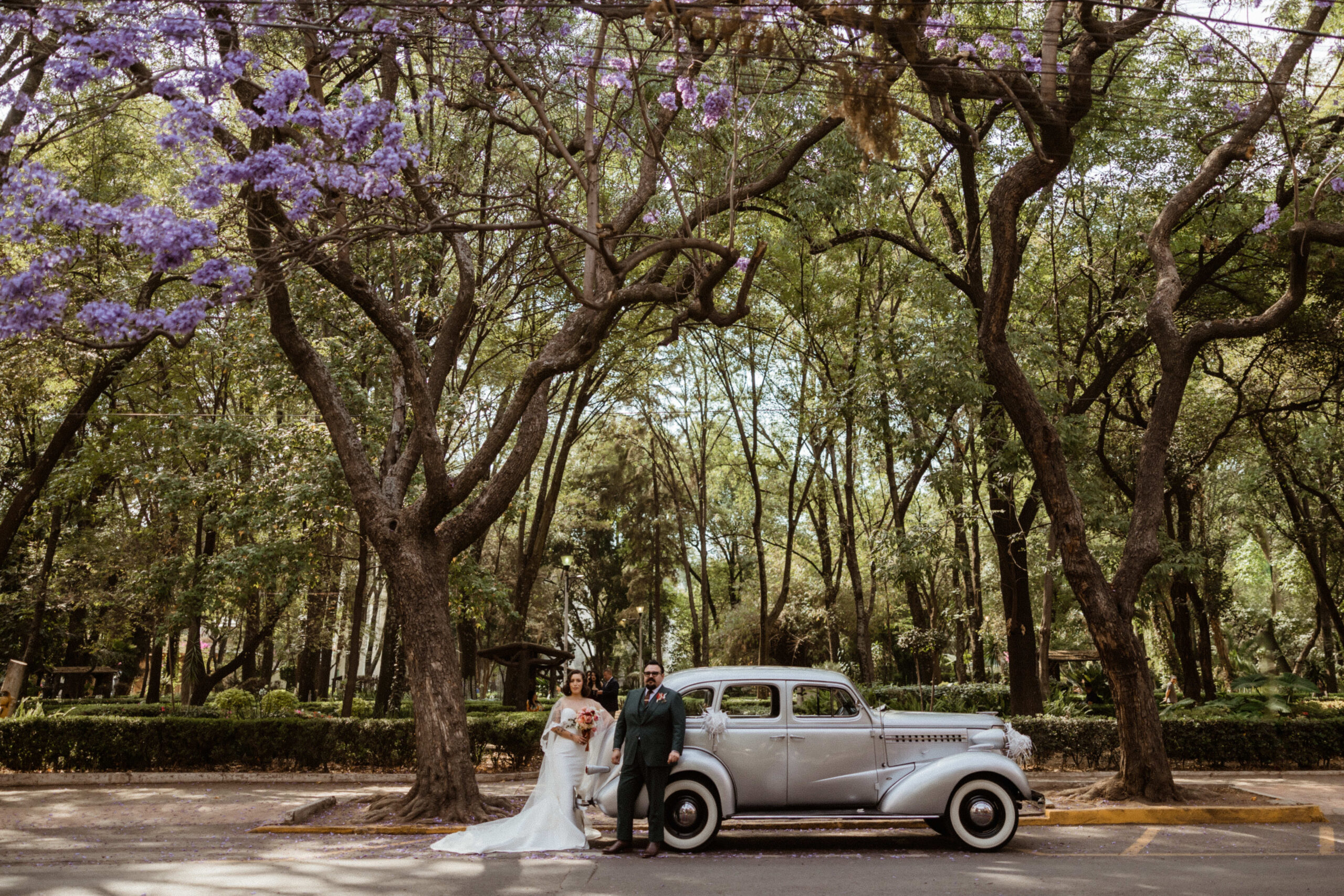 Beautiful bride and groom pose with their getaway car after their Sobremesa wedding