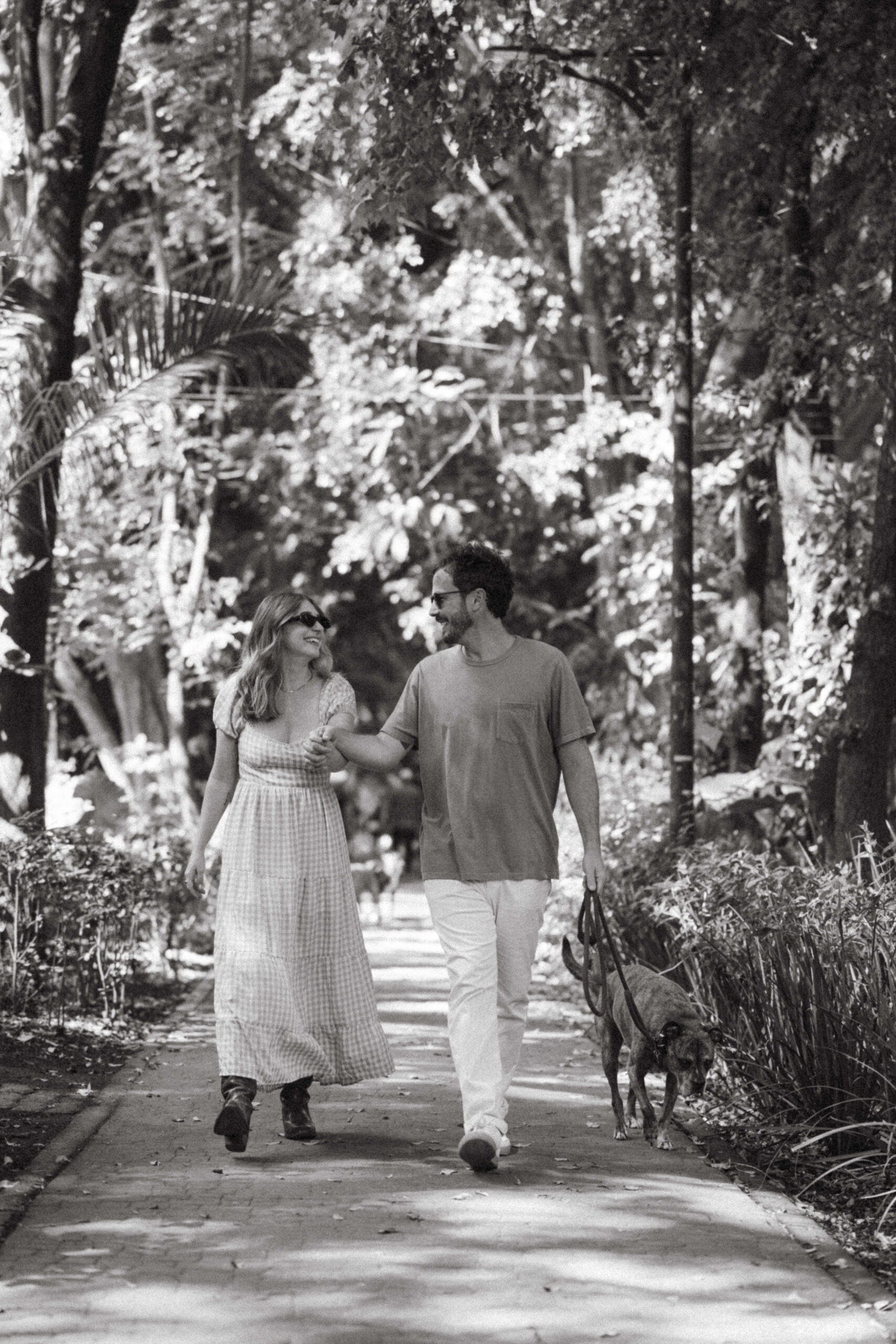 black and white photo of man and woman walking in garden with their dog 