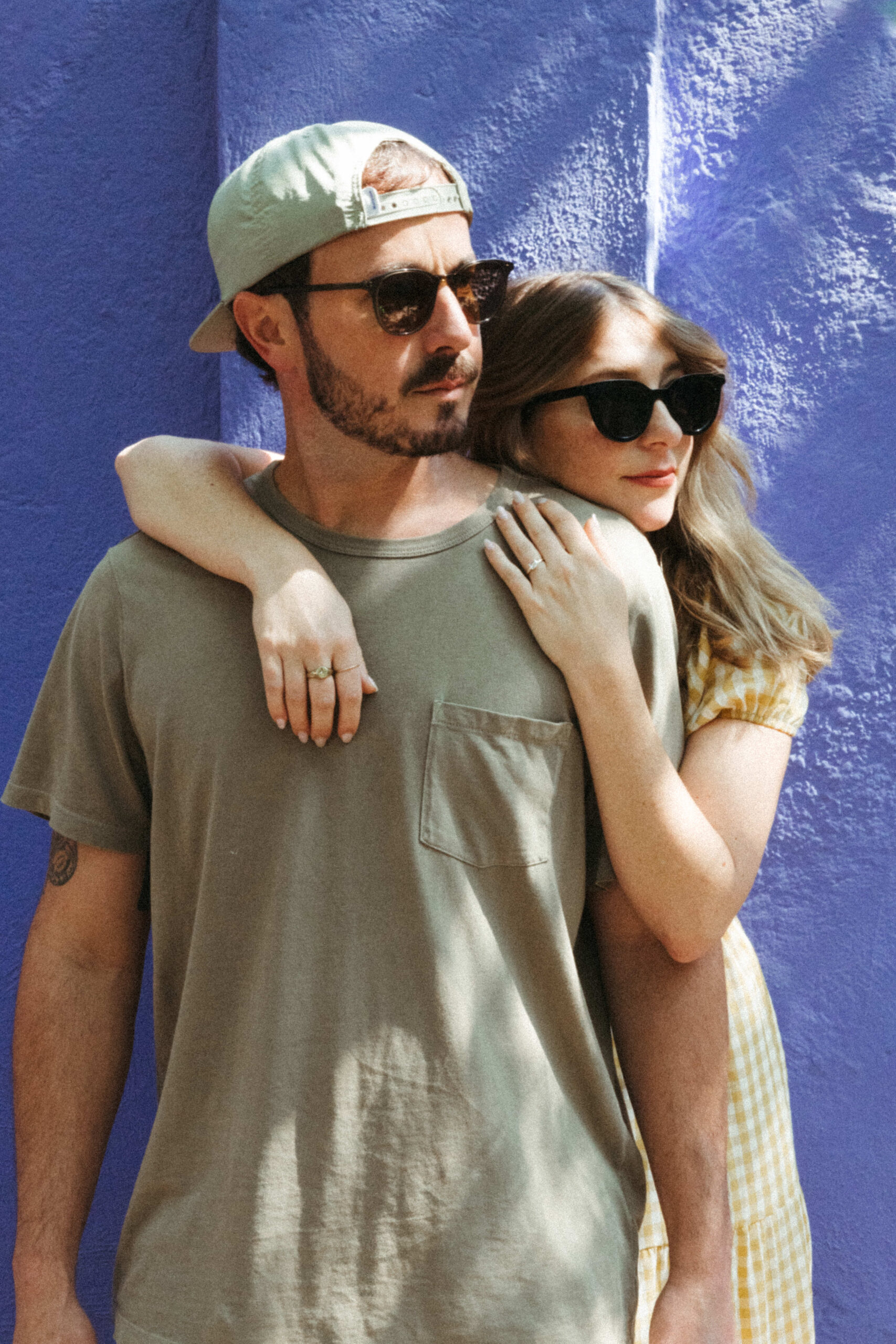 man and woman looking in the distance while wearing sunglasses in front of blue building