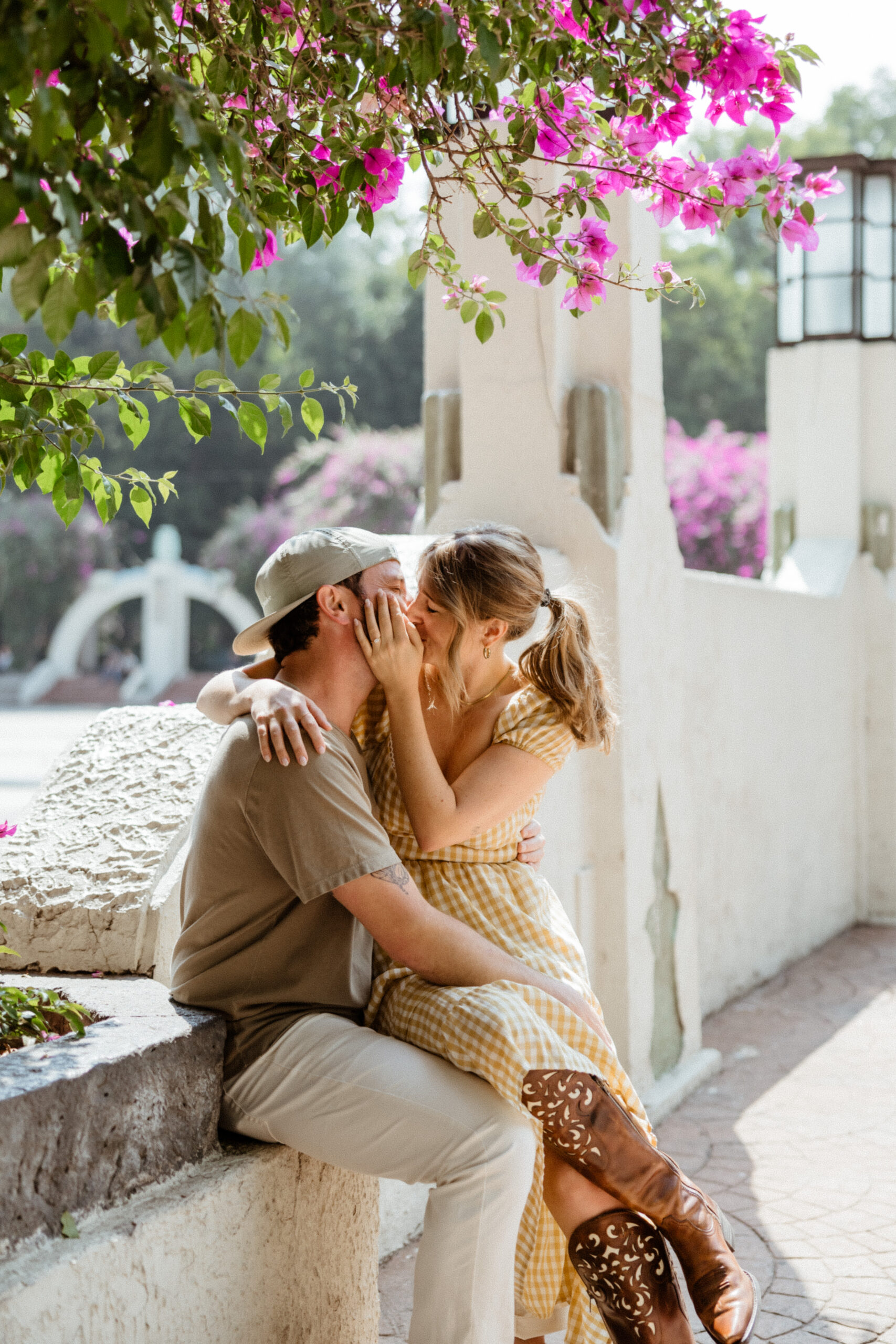 man and woman sitting down sharing a kiss under a tree of pink flowers