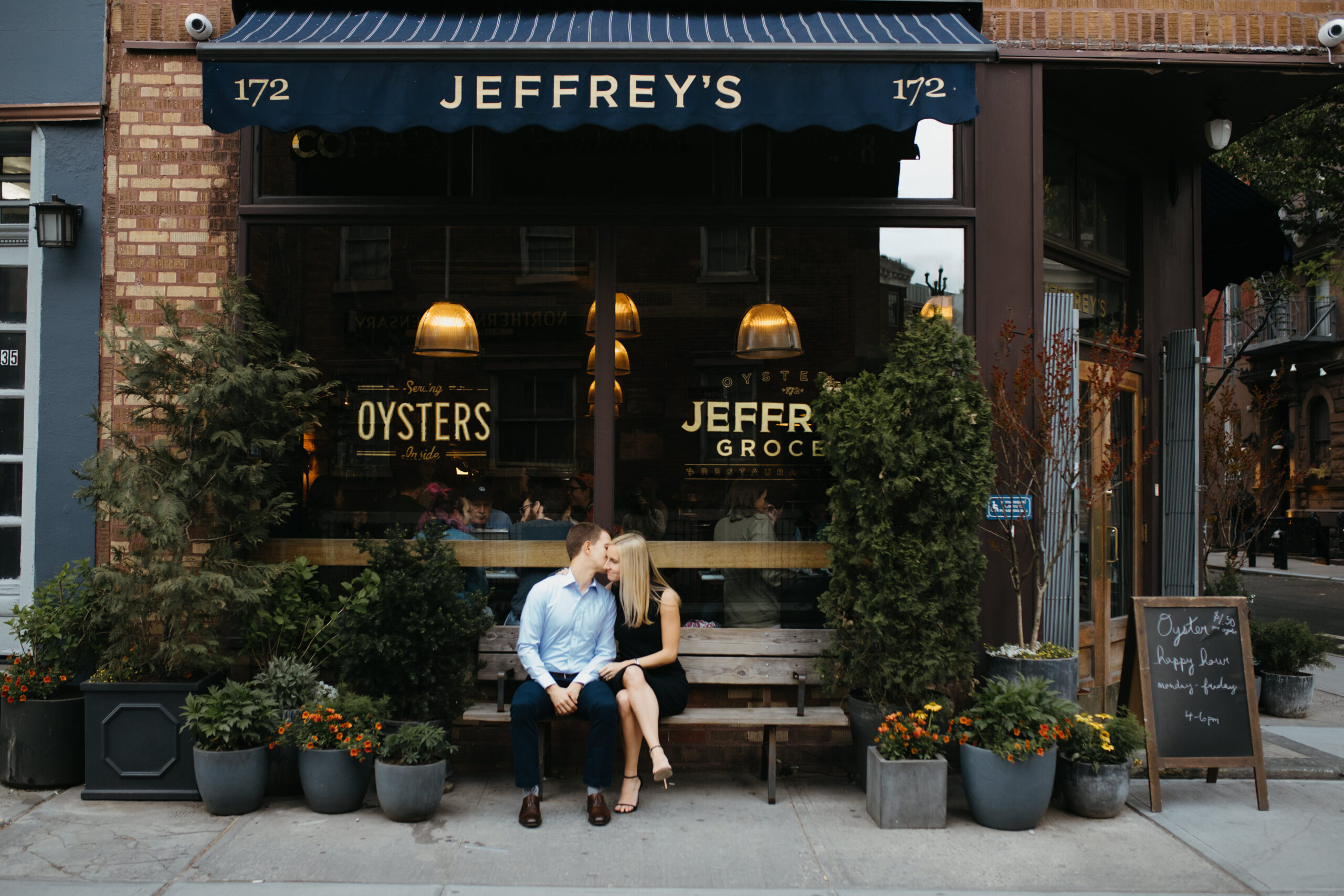 Stunning couple sit outside Jeffrey's grocery in West Village, New York during their dreamy Winter engagement photoshoot