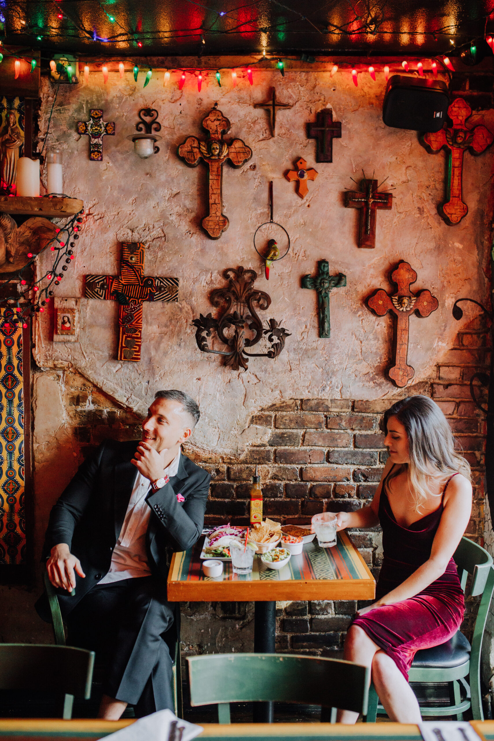Stunning couple sit in front a cross covered wall in during their dreamy engagement photos
