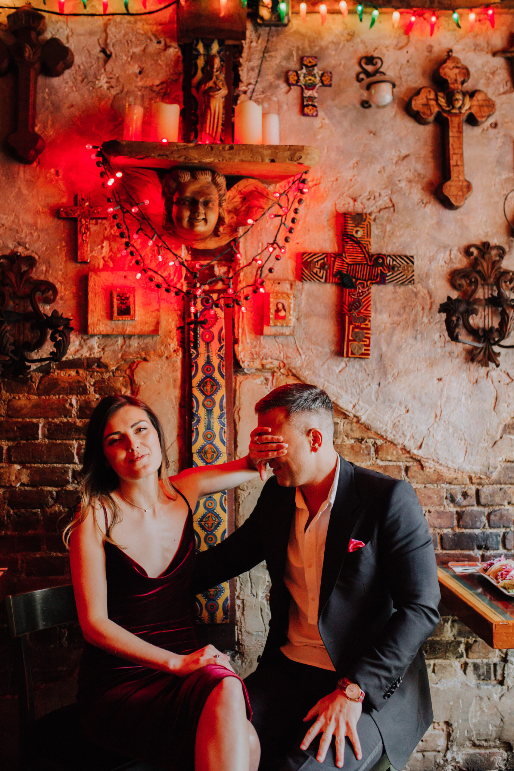 Beautiful couple sit in front of wall of crosses during their dreamy NYC engagement photoshoot