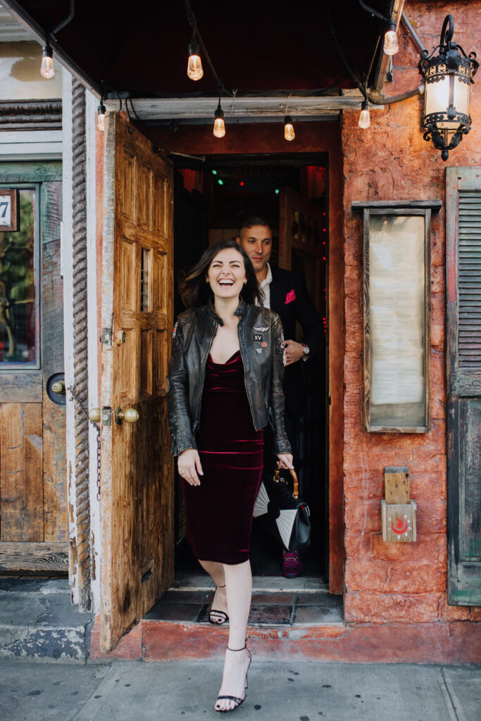 fiance laughing in a velvet maroon dress walking out of the bar. 
