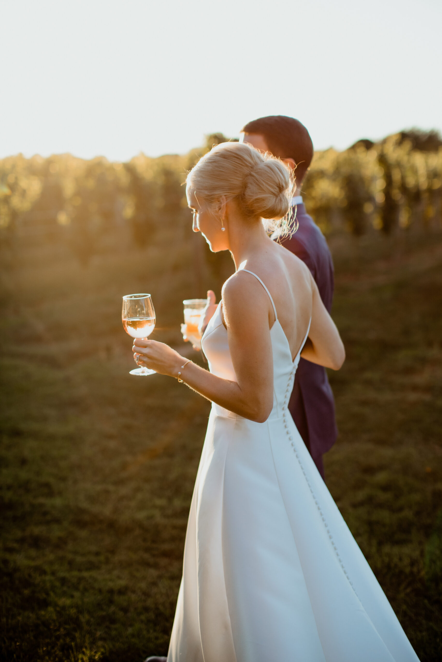 Stunning bride and groom walk in the vineyard while sharing a glass of wine