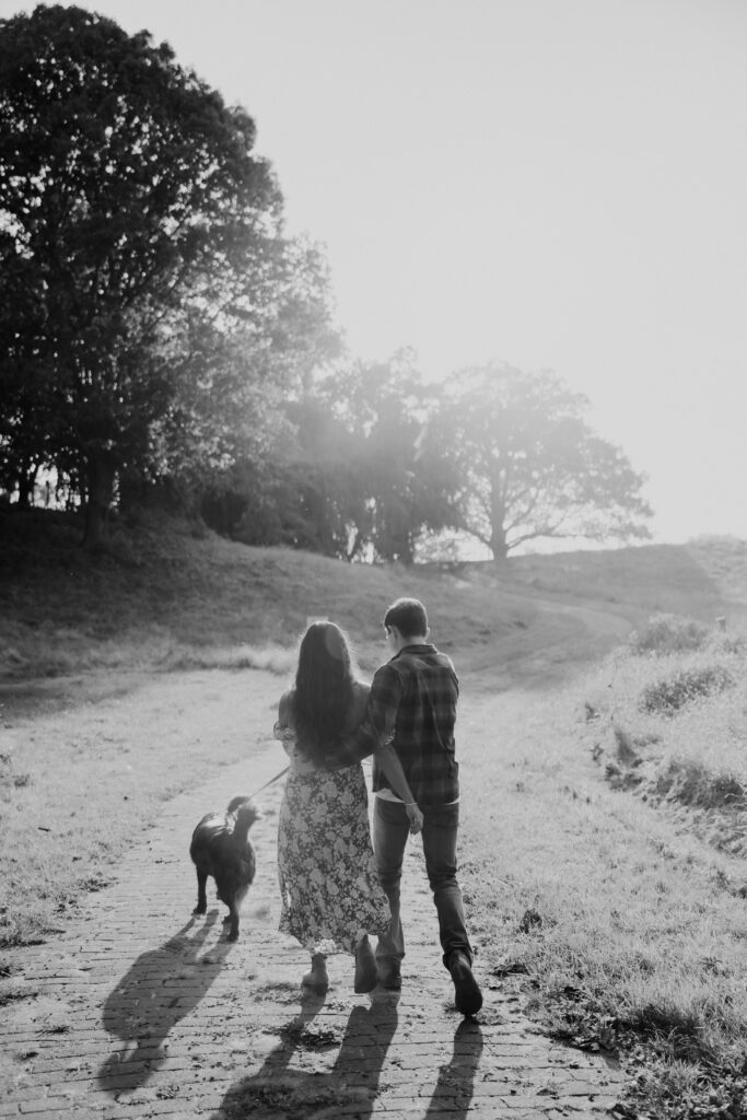 beautiful couple walk on a country road with their dog during their casual engagement shoot