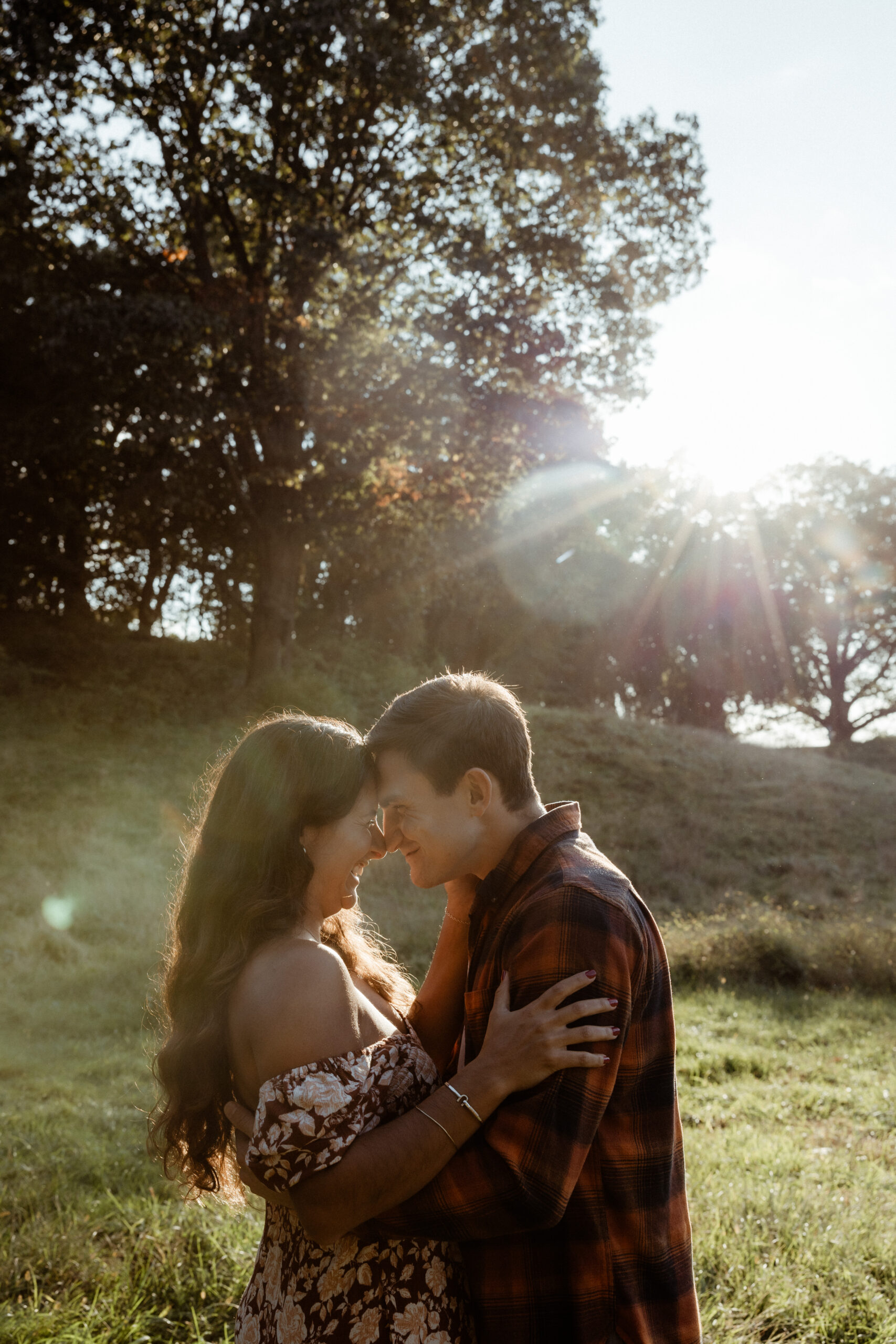 Couple embrace each other sitting in the field during their casual engagement photo shoot