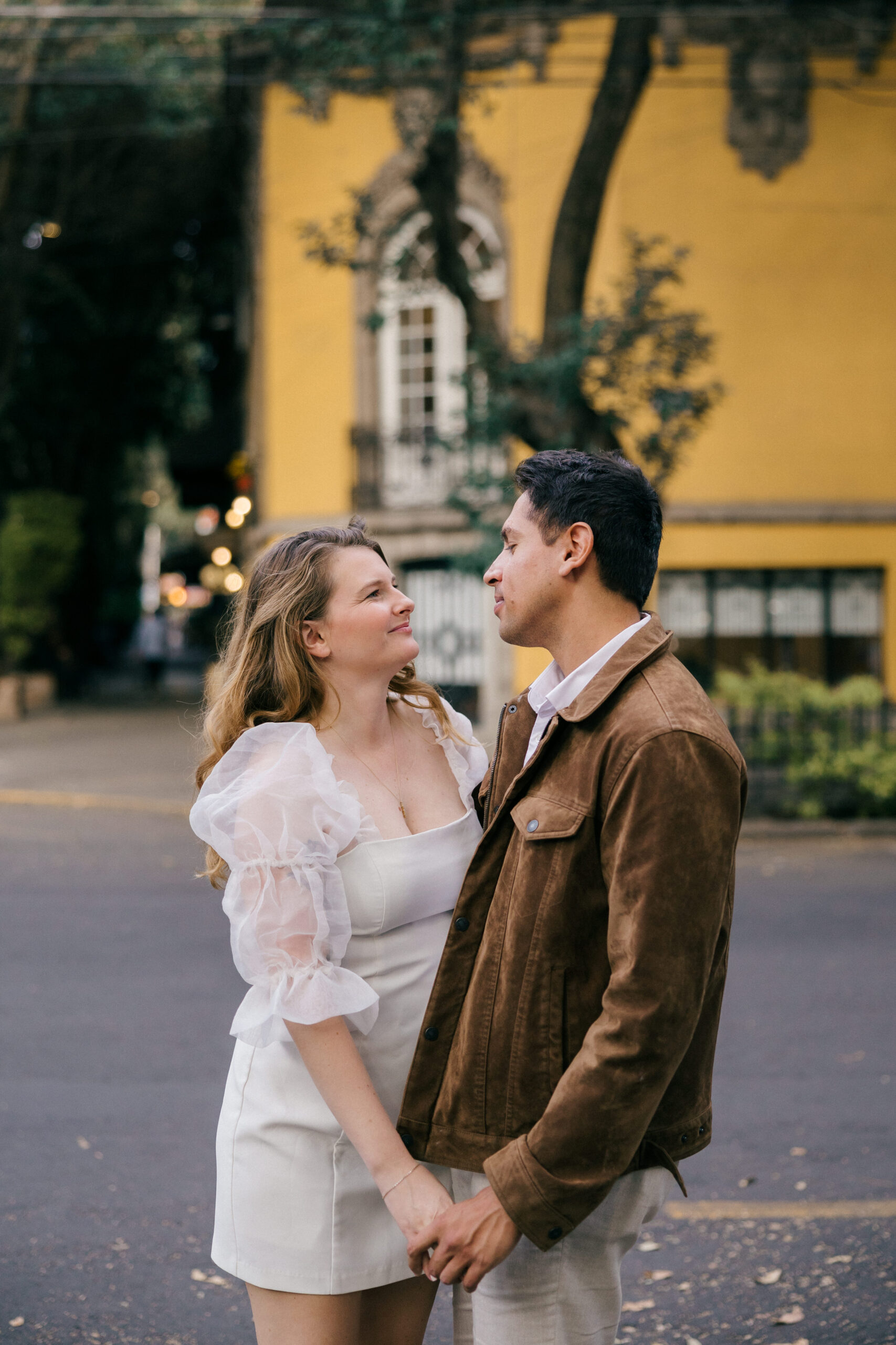 Beautiful couple pose together on the Mexico city streets with a yellow building in the background