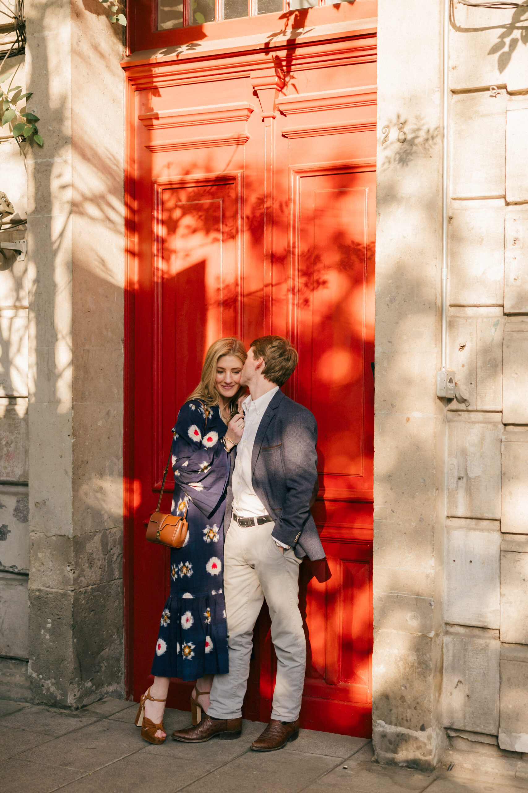 Stunning couple share a kiss on the cheek in front of a red door in Mexico City