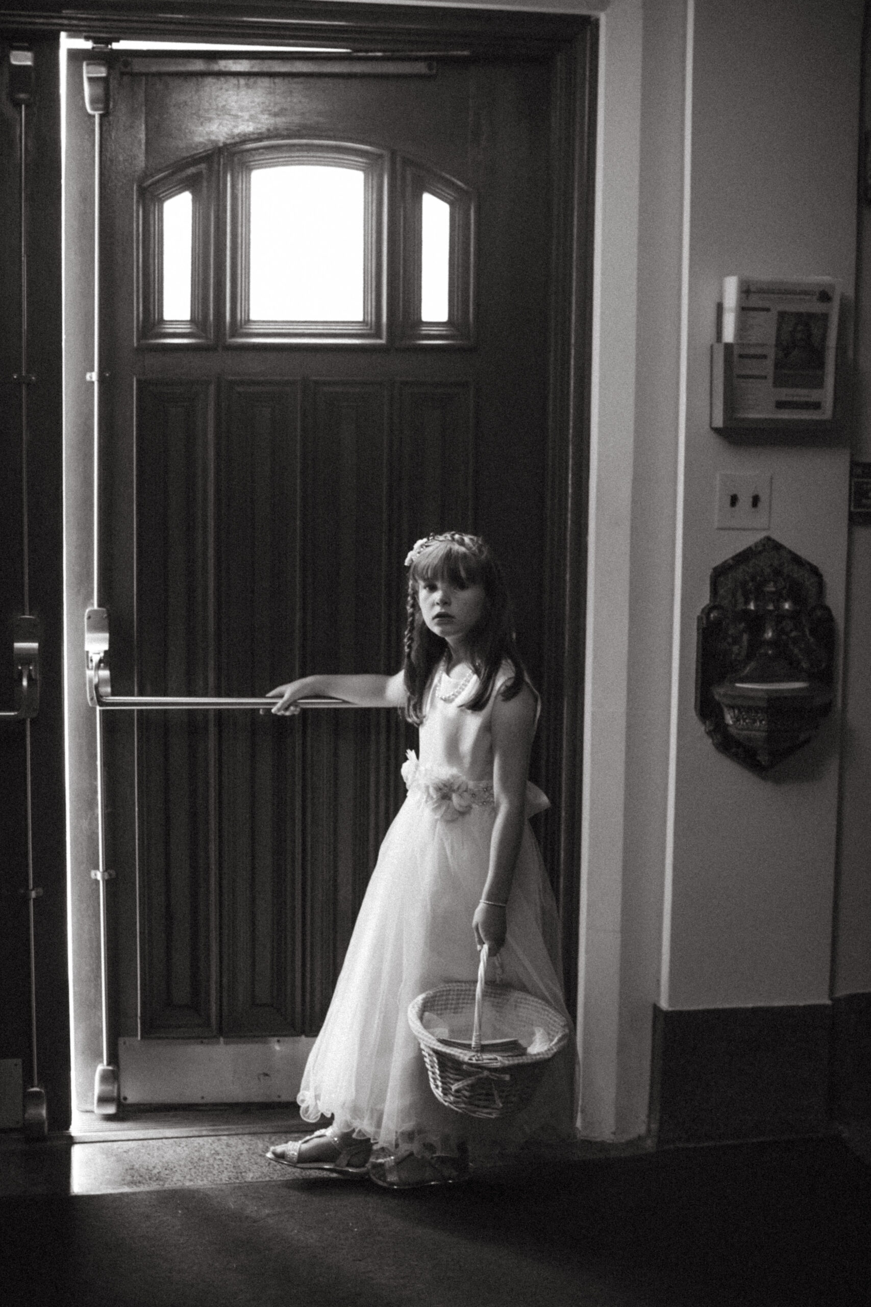Flower girl poses with her basket at the church door as she awaits the start of the ceremony 