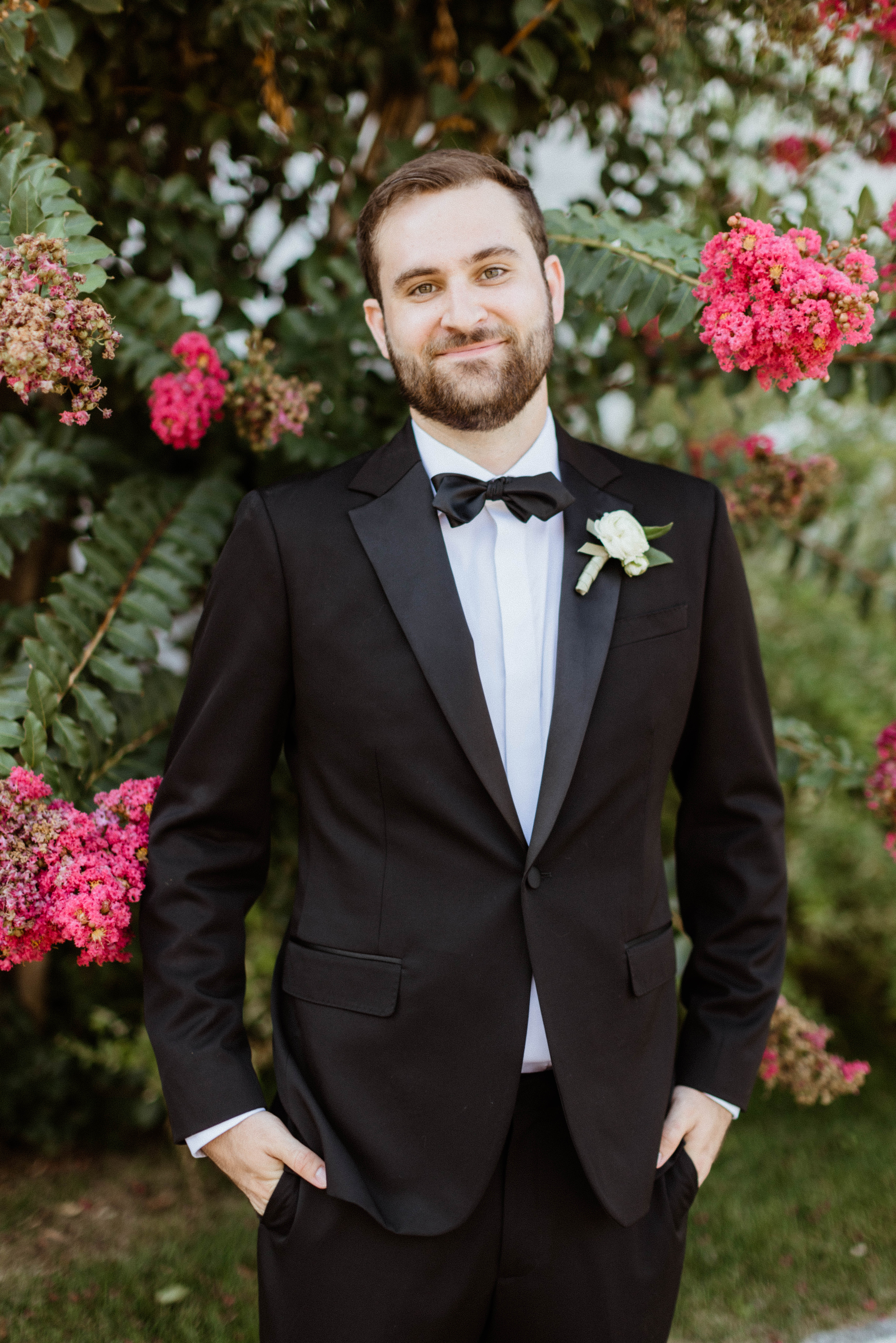 Groom poses with stunning pink flowers in the background 