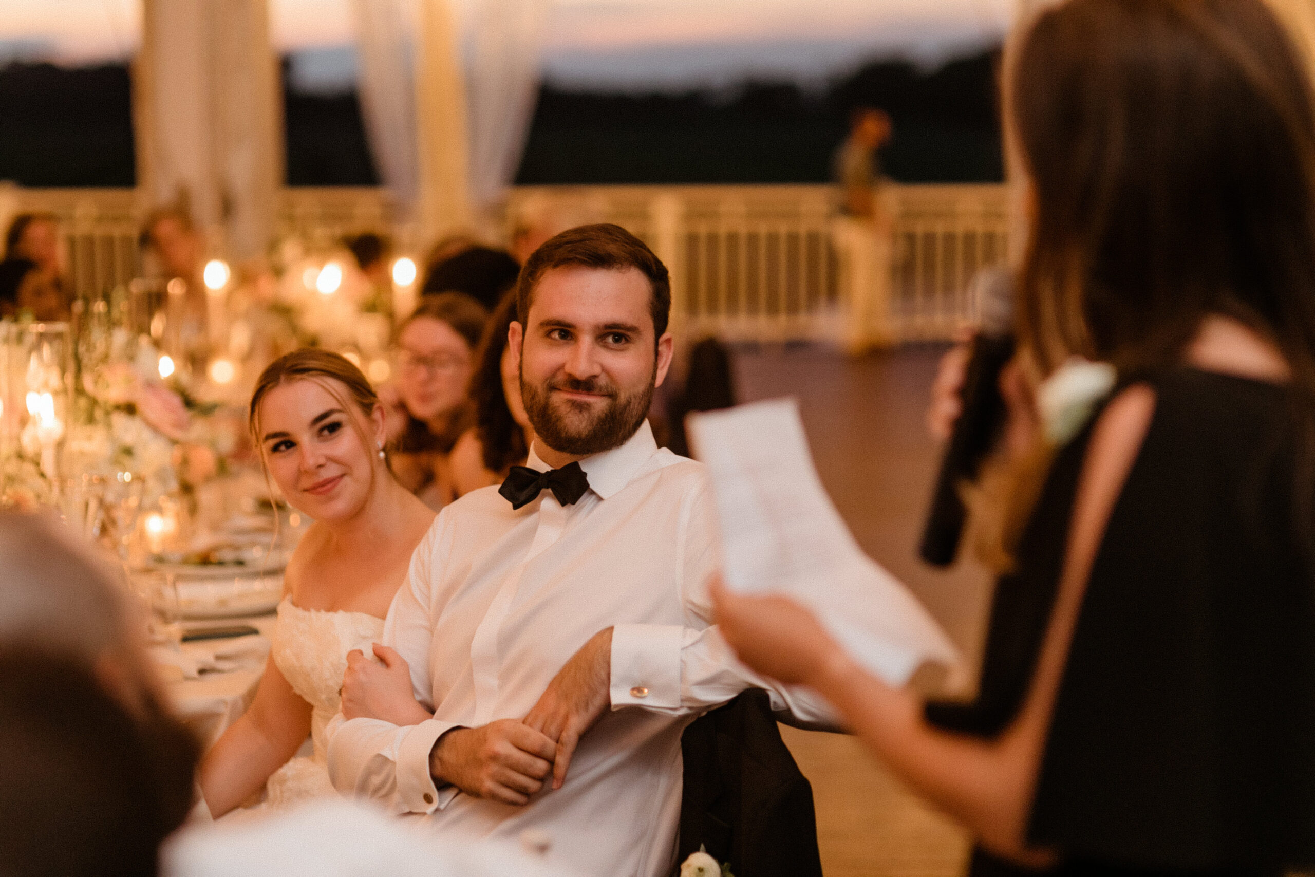 Bride and groom look on as their wedding party gives emotional toasts