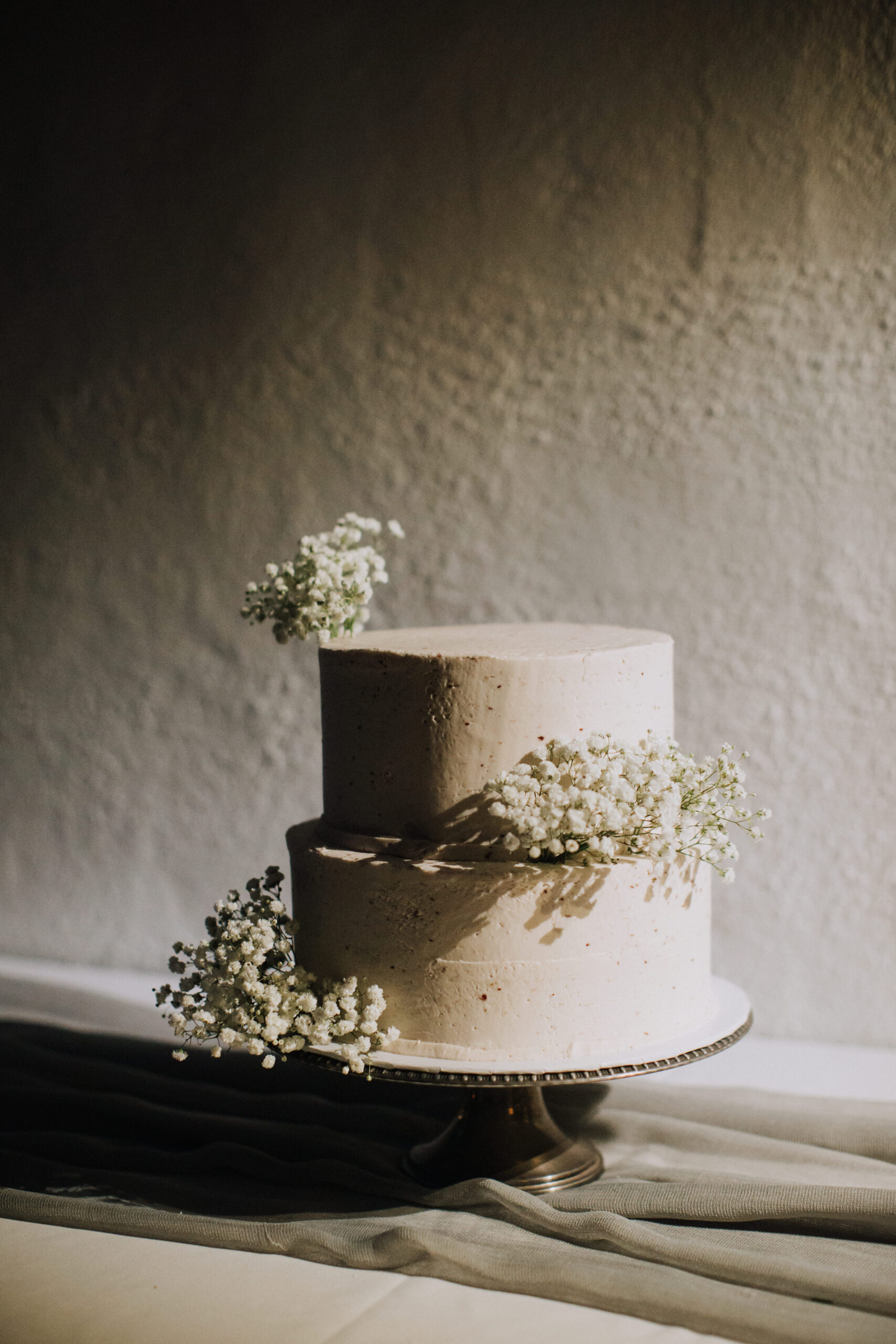 wedding cake sits in the sunlight flanked by white florals 