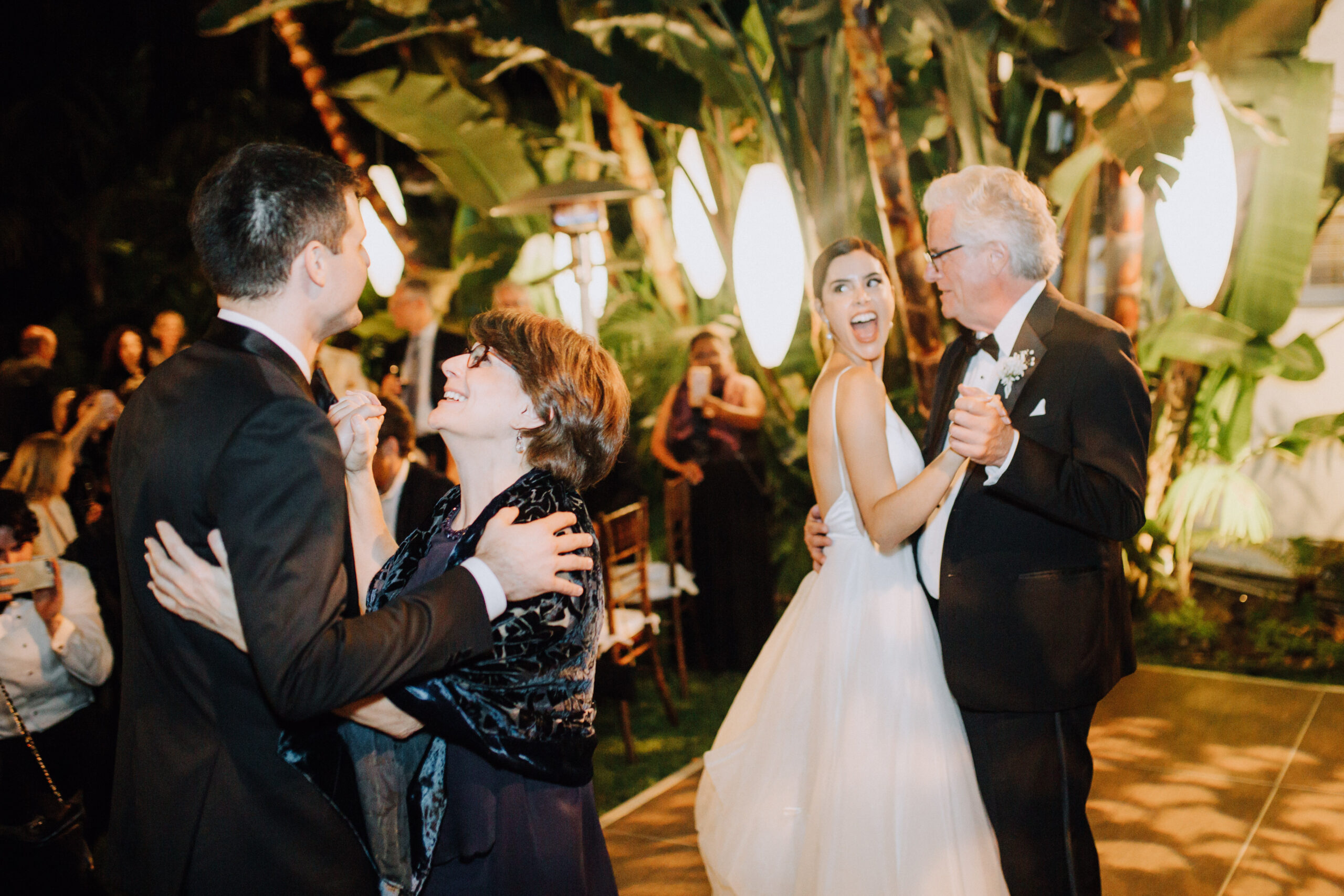 bride shares a dance with her dad as her new husband share a dance with his mom