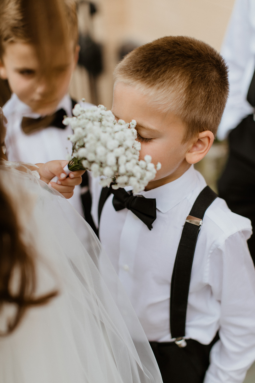 boys take turns sniffing the white wedding flowers