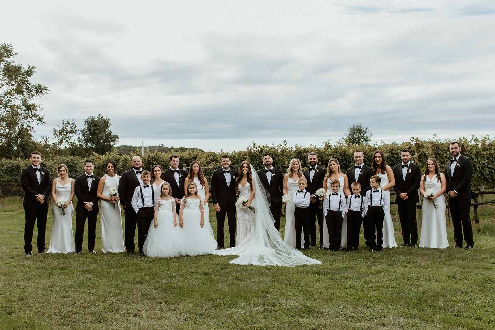 wedding party poses for a photo with the vineyard in the background