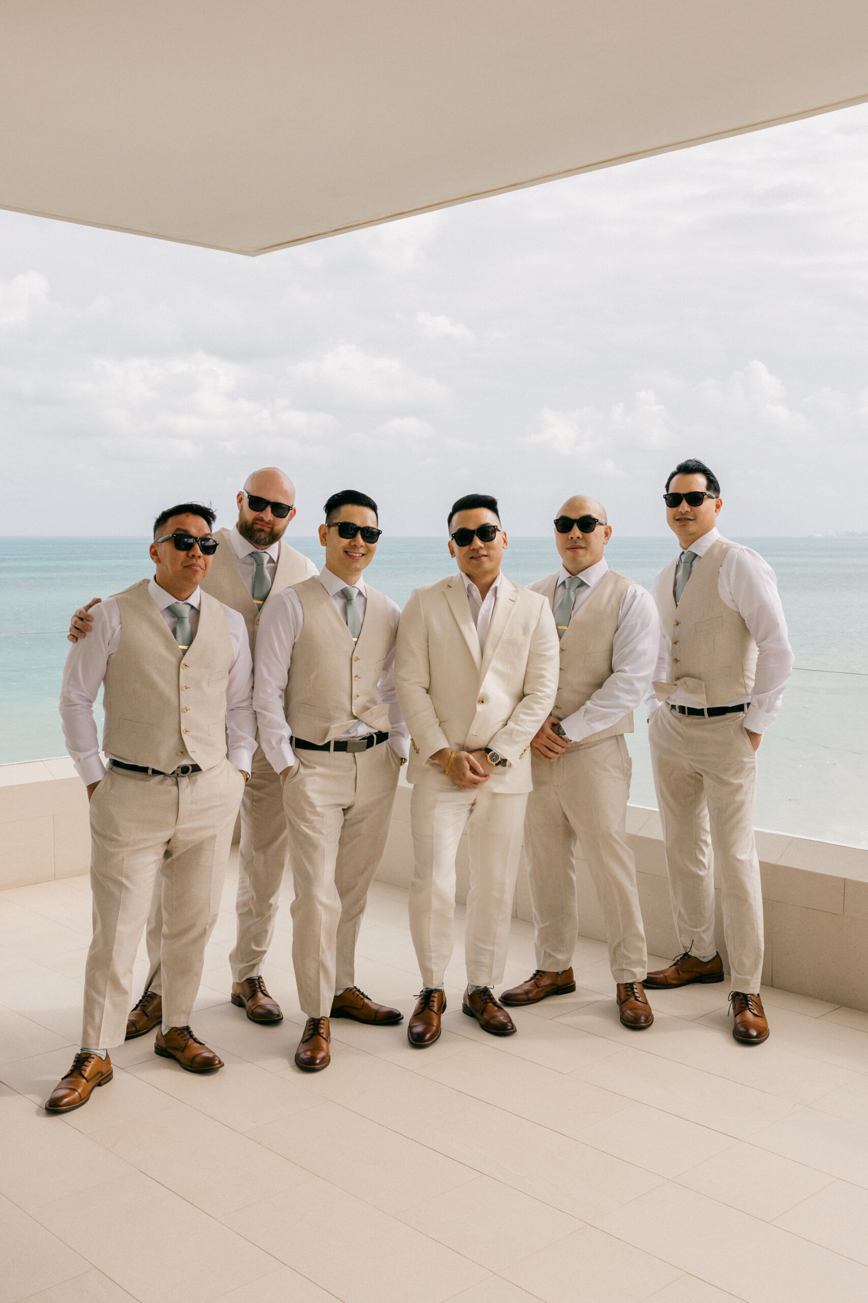 groom and groomsmen pose for a photo with the ocean in the background