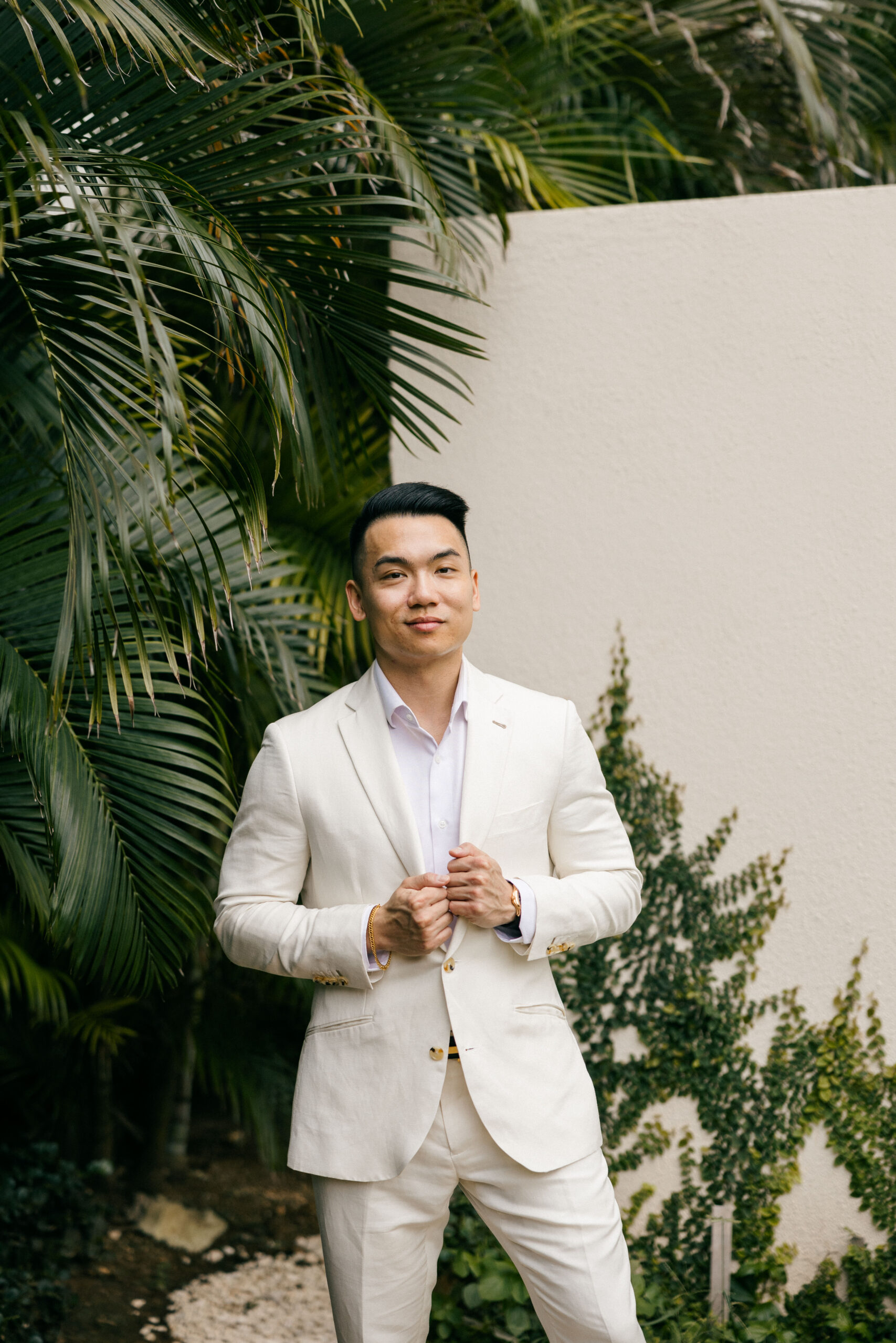 groom poses for a photo with tropical plants in the background