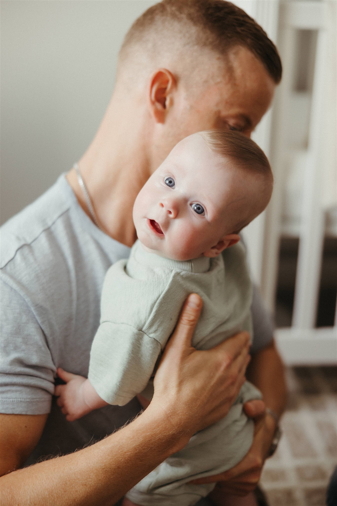 dad poses for a photo with his newborn child during their in home family photoshoot