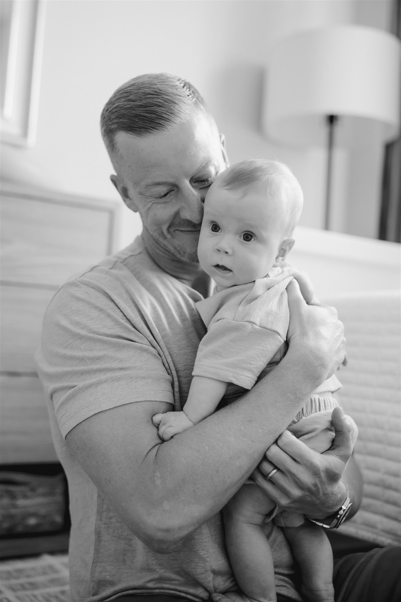 dad poses for a photo with his newborn child during their in home family photoshoot